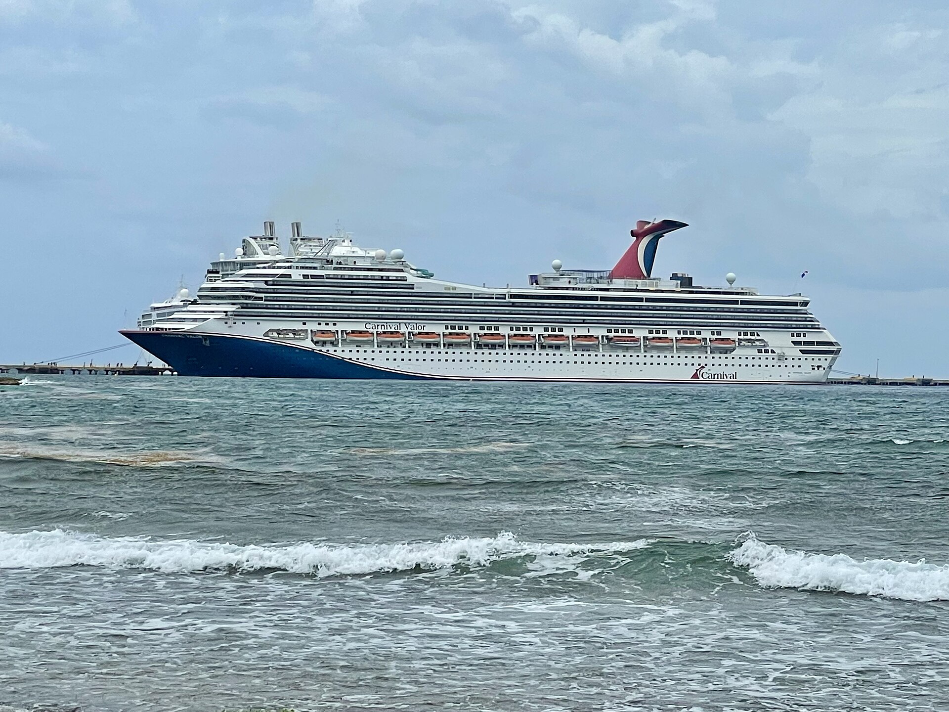 Carnival Valor cruise ship docked at Costa Maya, Mexico, with waves breaking in the foreground
