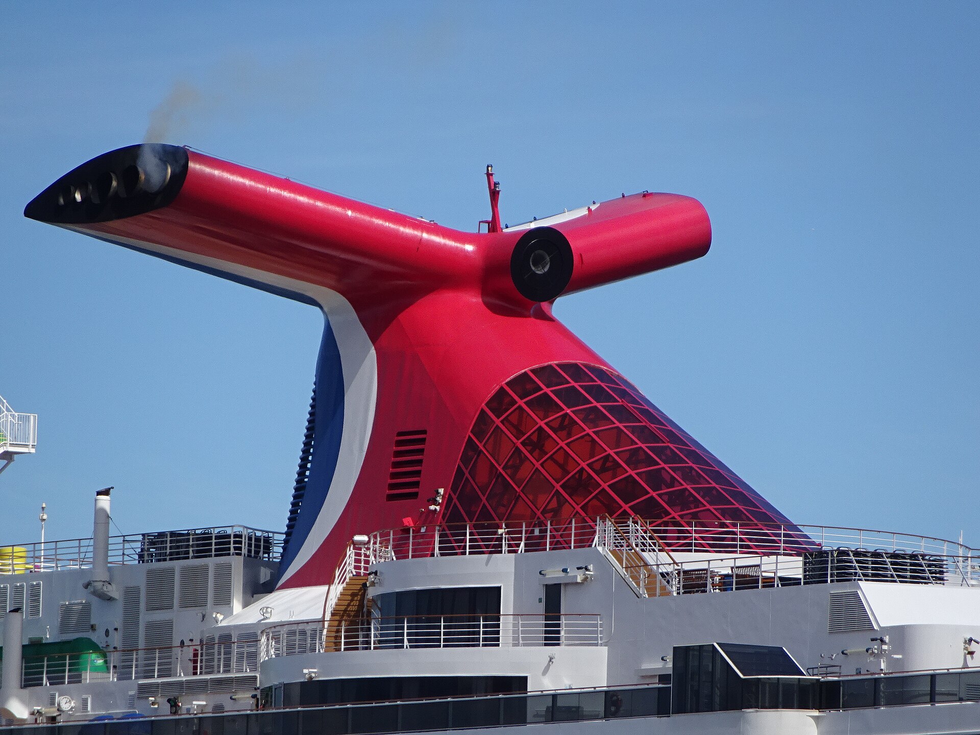Close-up of a red Carnival whale tail funnel against blue sky, with exhaust outlets at the tip of each wing