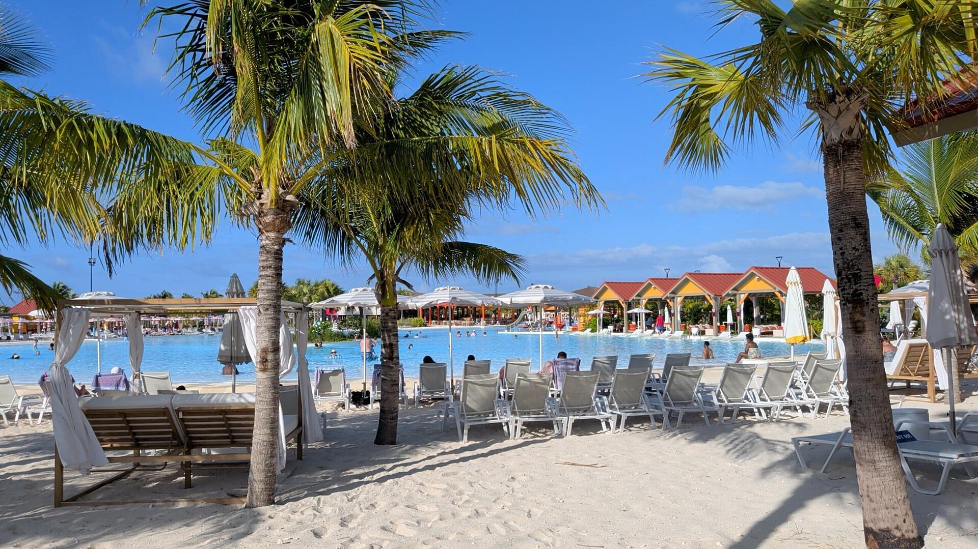 Palm trees, white loungers and shade umbrellas beside a lagoon at Carnival's Celebration Key in the Bahamas