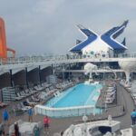Blue pool, sun loungers and the orange Magic Carpet platform on the pool deck of Celebrity Beyond