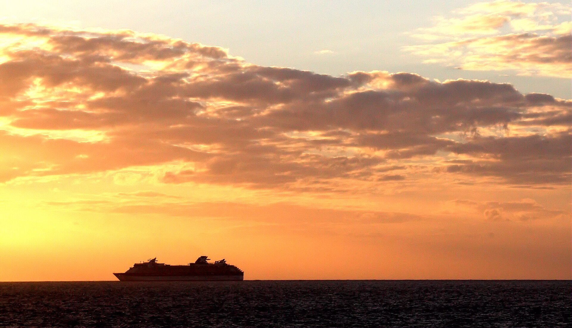 Silhouette of the cruise ship Celebrity Summit on the horizon under an orange and gold sunset sky off Grenada