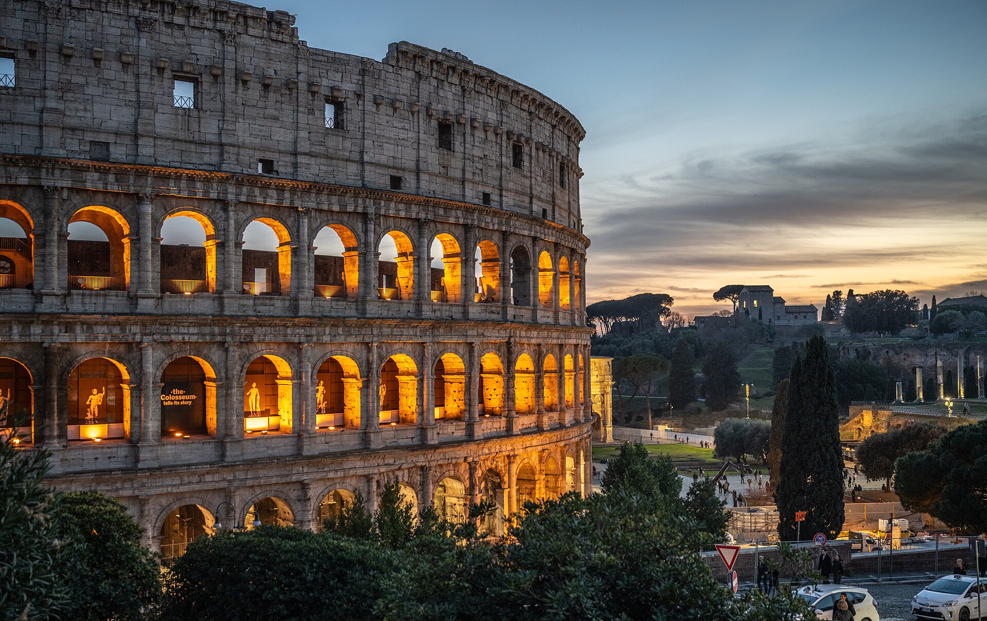 The Colosseum in Rome at dusk, its arches lit gold against a blue and orange sky