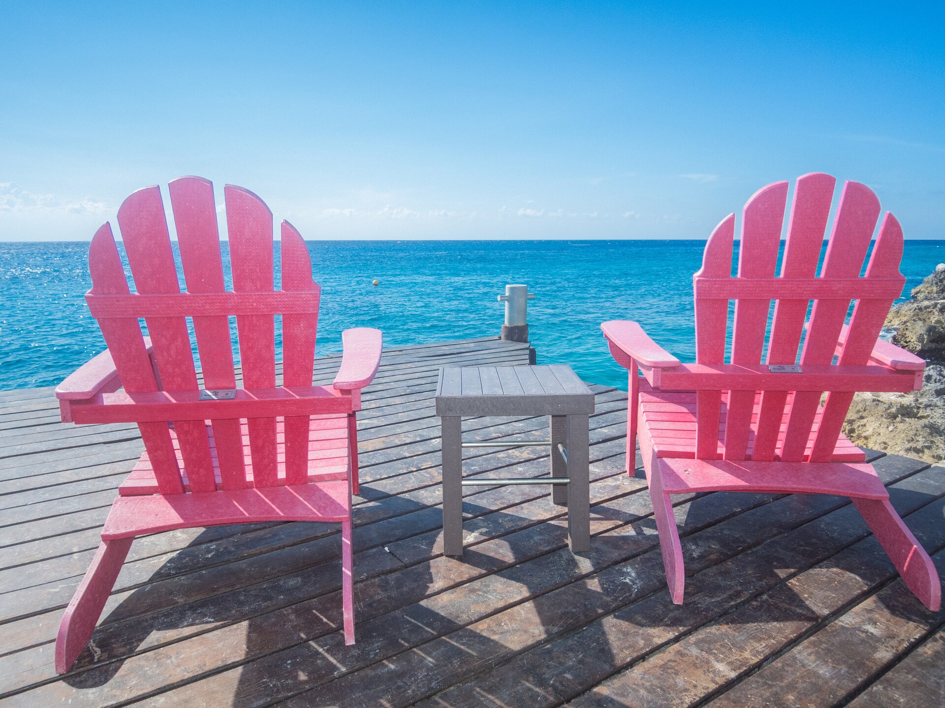 Two pink Adirondack chairs on a wooden dock facing turquoise Caribbean water in Cozumel