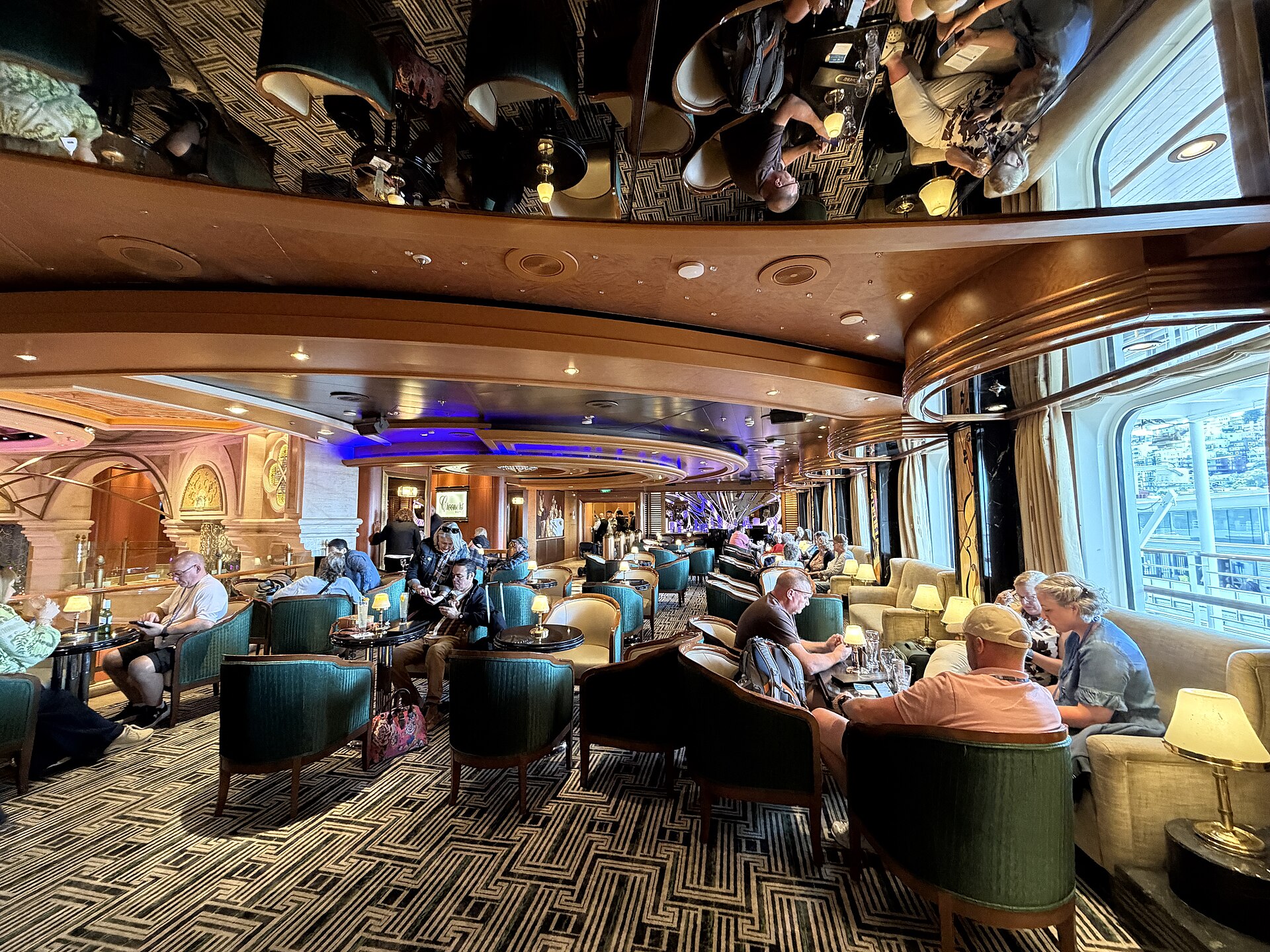 Guests relaxing in armchairs at the Crooners lounge on Ruby Princess, lit in blue with sea windows