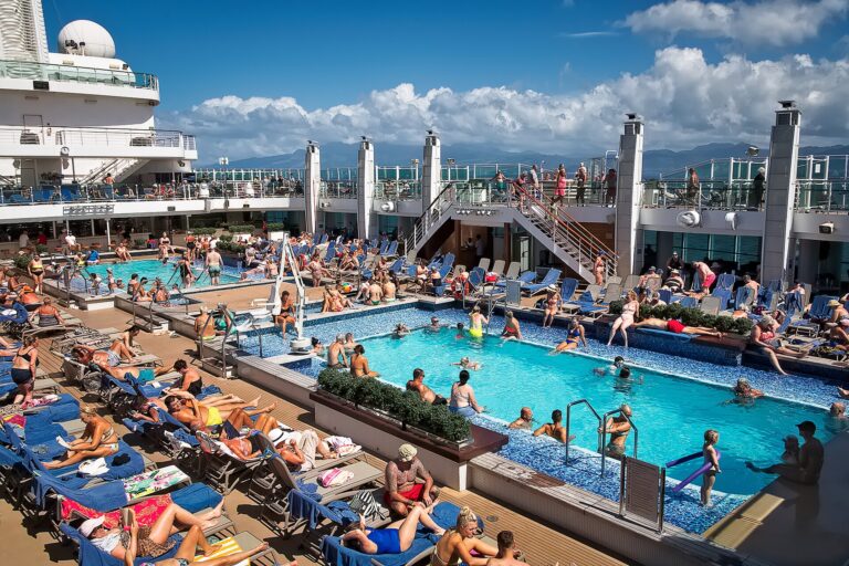 Sunbathers on blue loungers around a bright blue pool on the deck of the cruise ship Britannia under a sunny sky