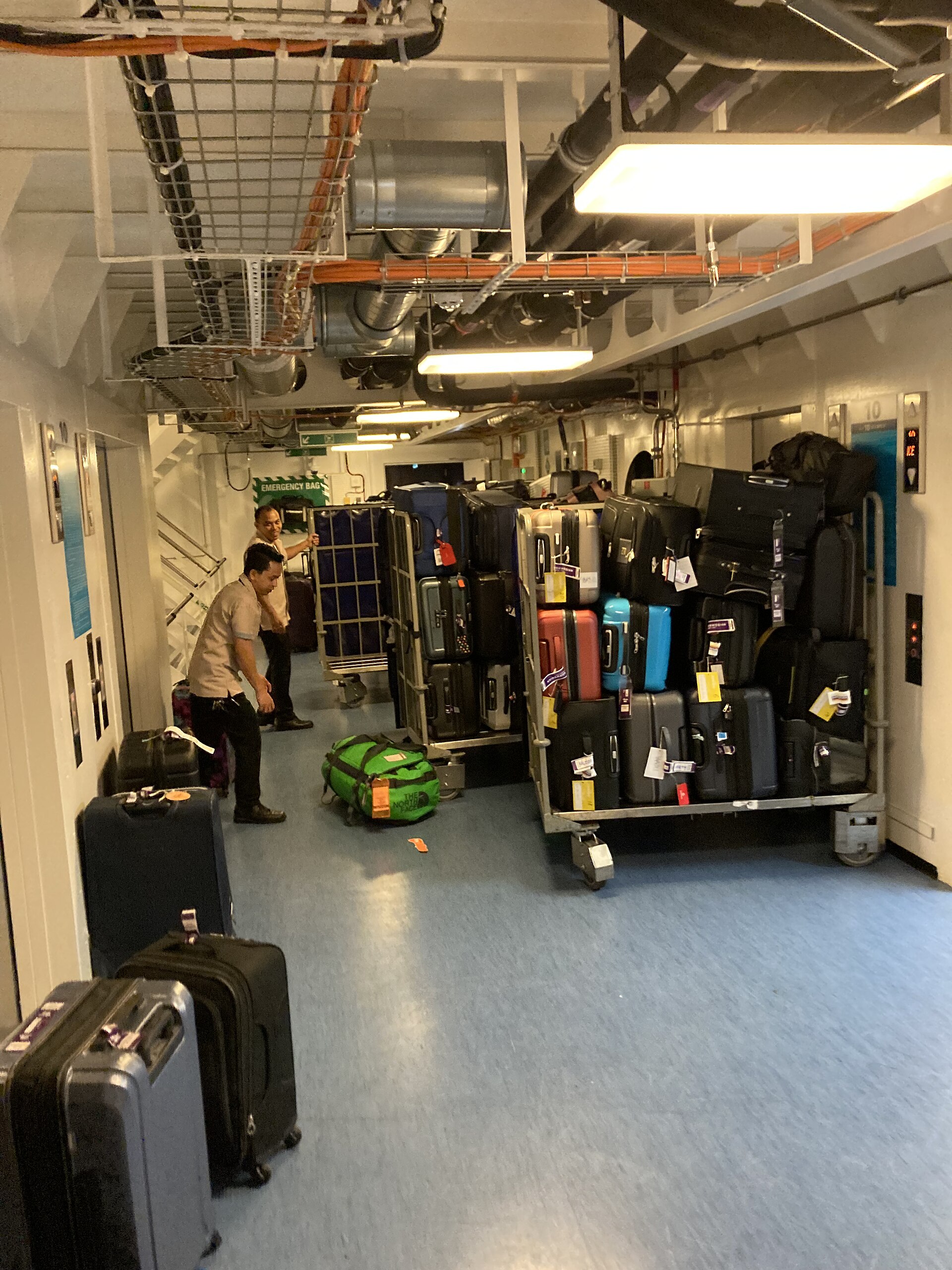 Crew members sorting racks of colourful suitcases with luggage tags in a crew corridor on a cruise ship
