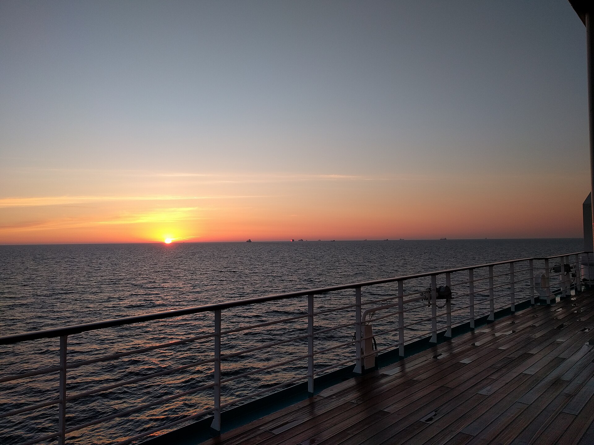Orange sunset over the open sea seen from the teak deck and railing of a cruise ship