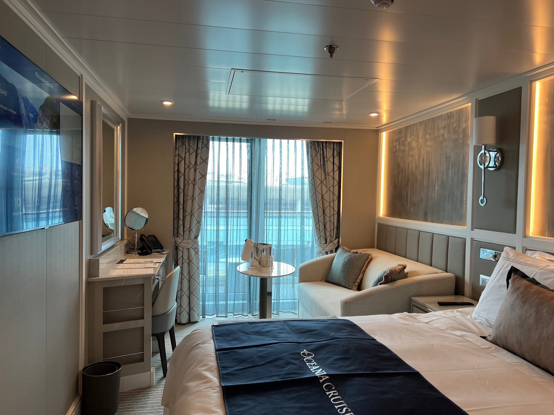 Bright veranda cabin on the cruise ship Oceania Vista with panelled walls, a sofa and a balcony door