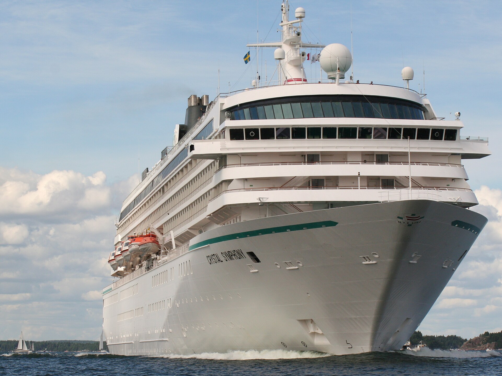 The white cruise ship Crystal Symphony sailing head-on towards the camera under a blue sky with clouds