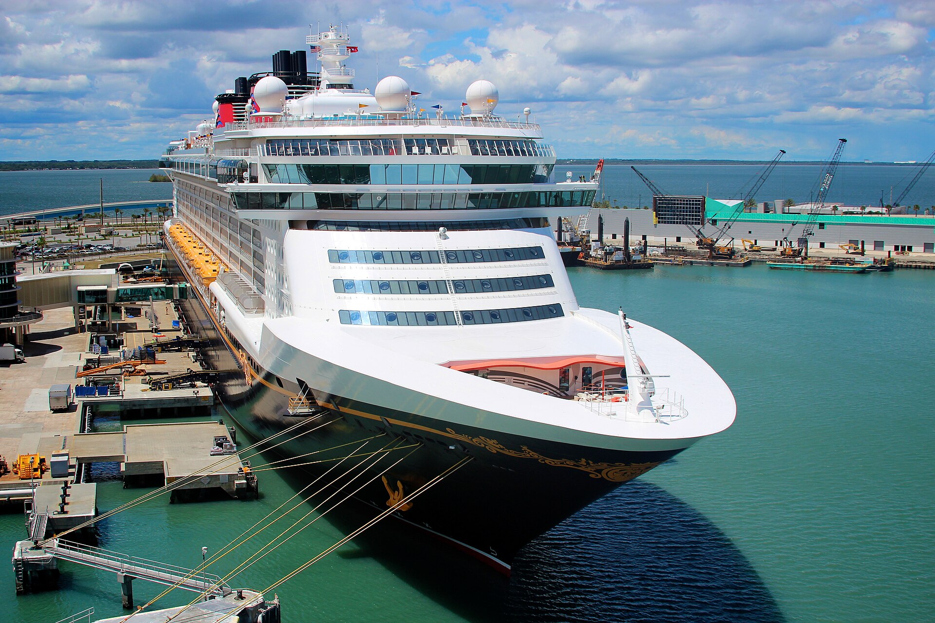 A Disney Cruise Line ship moored at the Disney cruise terminal in Port Canaveral, with green water and a blue sky