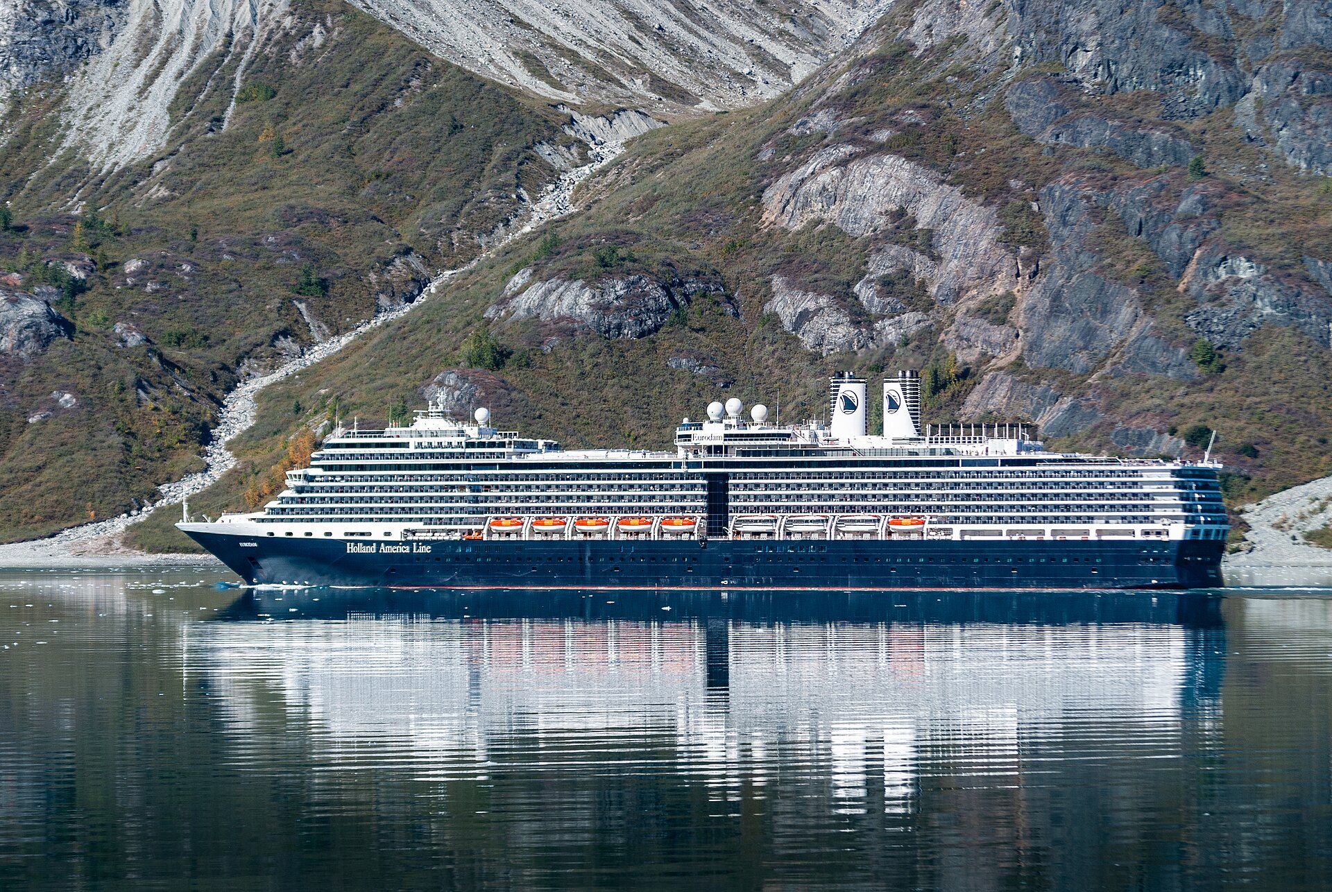 Holland America's Eurodam reflected in calm water at the entrance to Reid Inlet, Glacier Bay, with autumn-tinted slopes behind