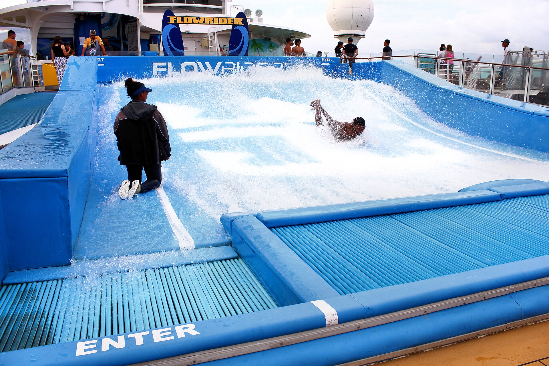 A passenger bodyboarding on the bright blue FlowRider surf simulator on Voyager of the Seas