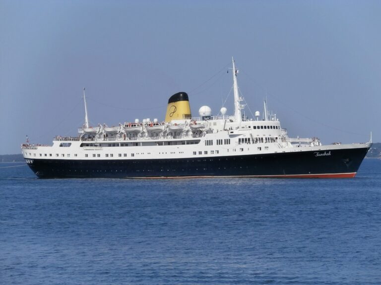 The classic liner Funchal, with a navy hull, white superstructure and yellow funnel, sailing on a bright blue sea