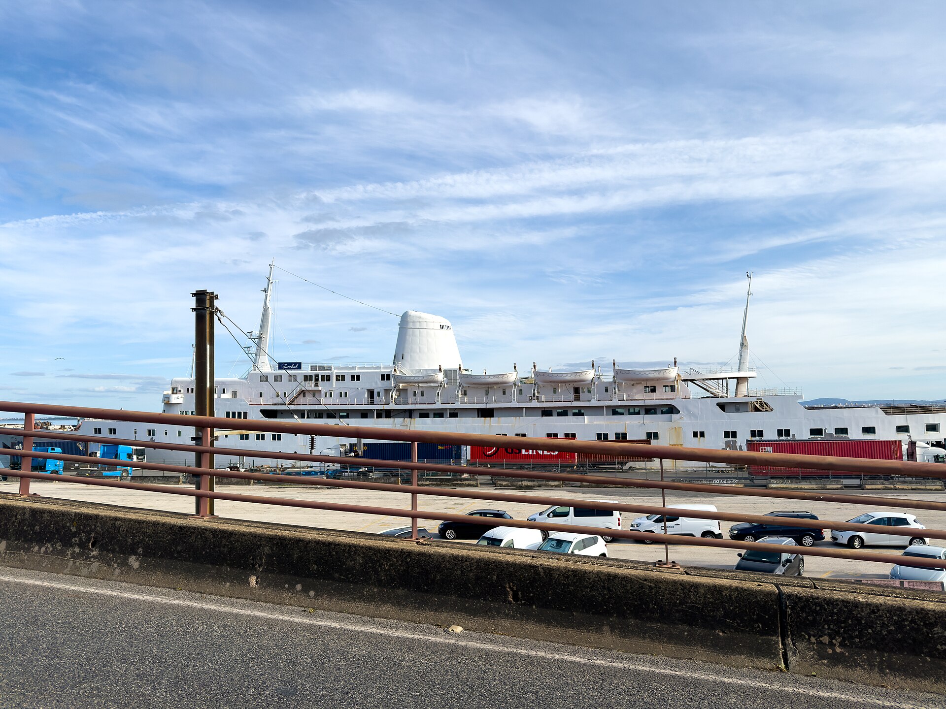Funchal in Lisbon in 2025, painted white with a bare white funnel, seen across a road and car park under a bright blue sky