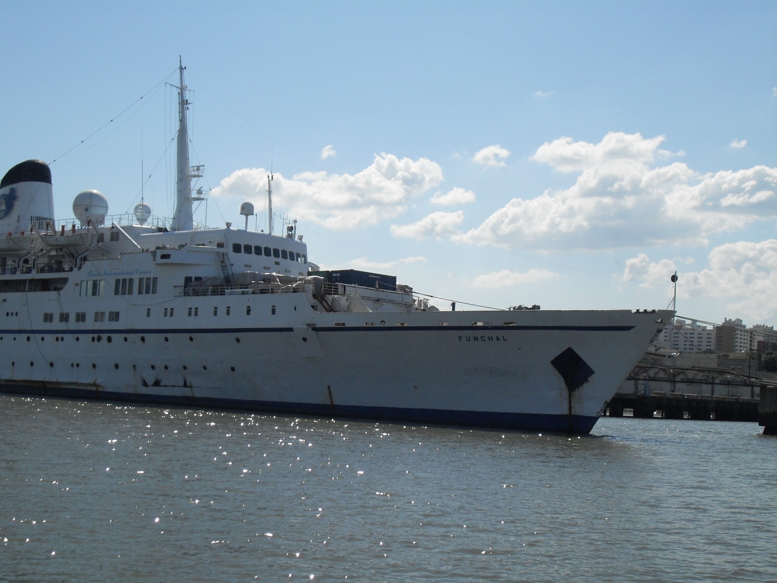 Funchal's white bow and navy waterline glittering in sunlight on the river in Lisbon, under blue sky and white clouds