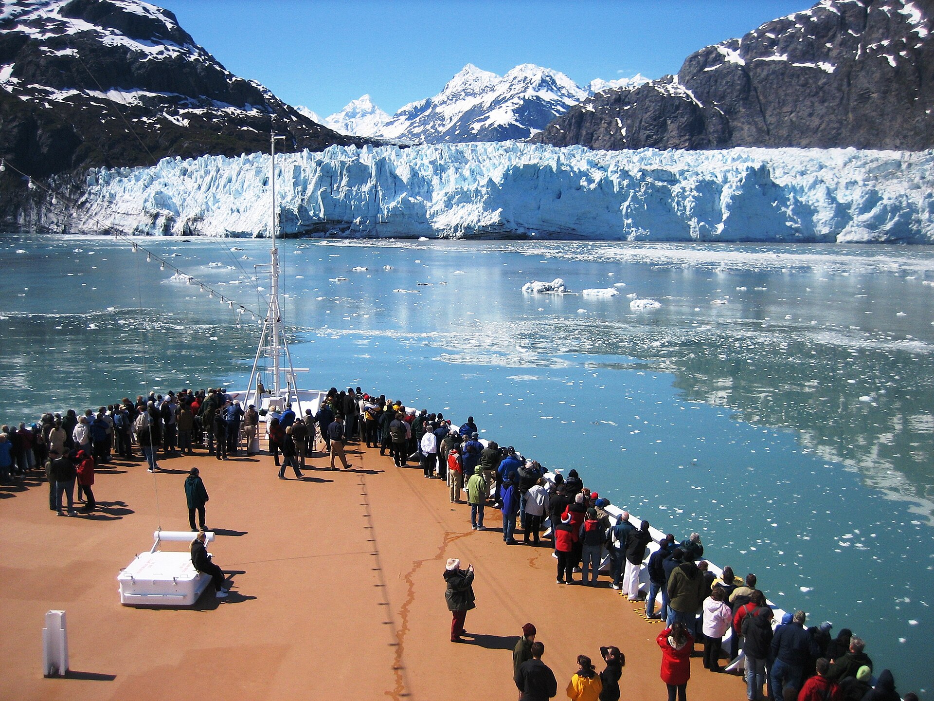 Cruise passengers in jackets and hats crowd the bow facing a tidewater glacier in Glacier Bay National Park