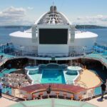 Turquoise pool and sun deck on Golden Princess with the giant Movies Under the Stars screen under a blue sky