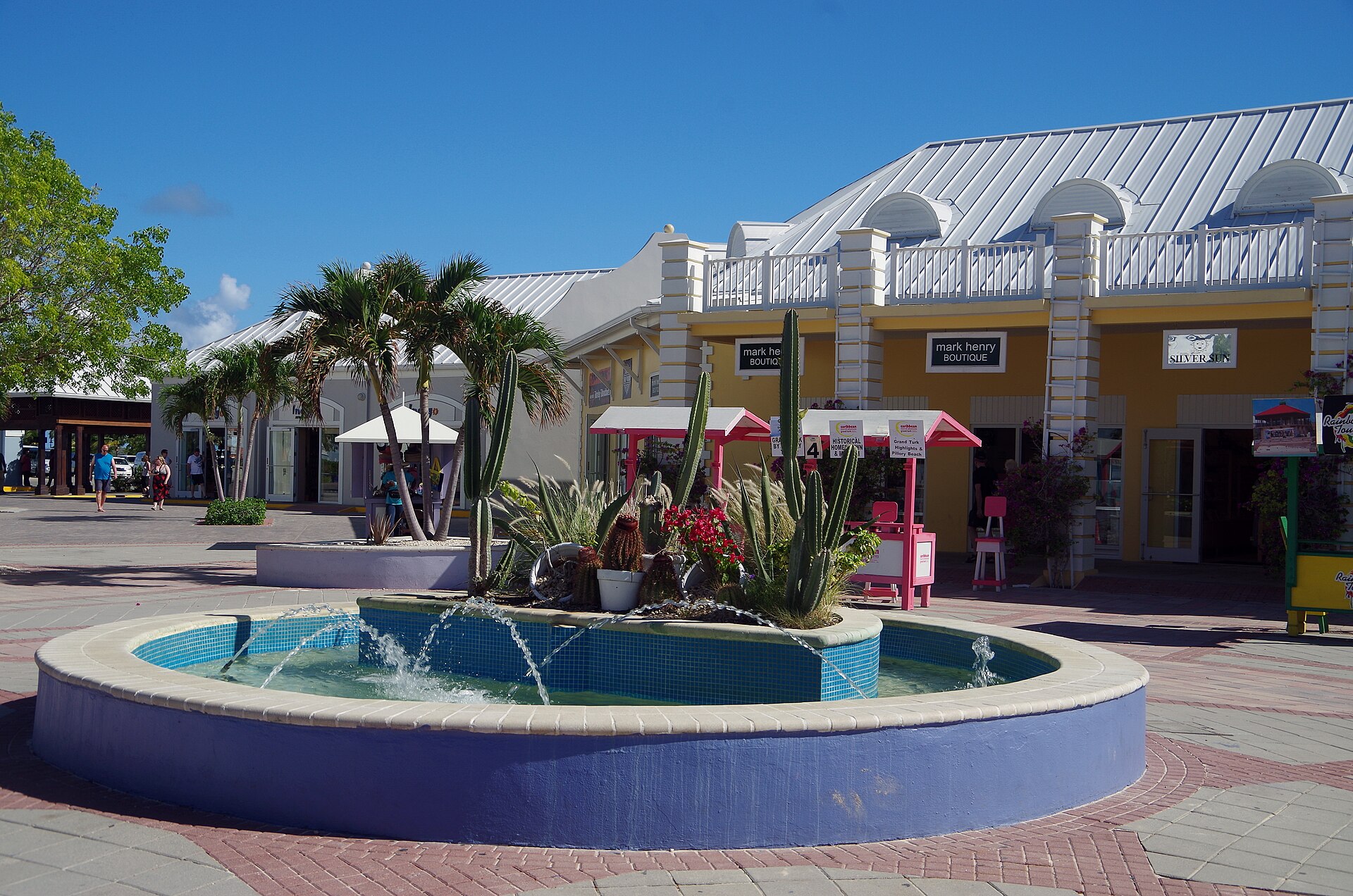 Colourful fountain, palm trees and yellow shops at the Grand Turk Cruise Center under a bright blue sky