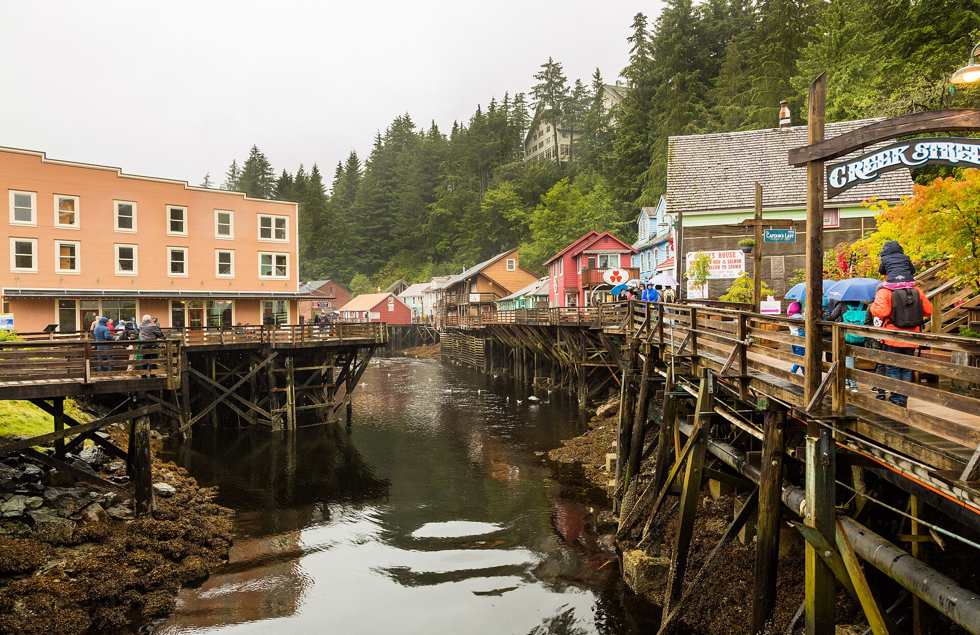 Visitors with umbrellas and rain jackets on the colourful boardwalk of Creek Street, Ketchikan, on a wet day
