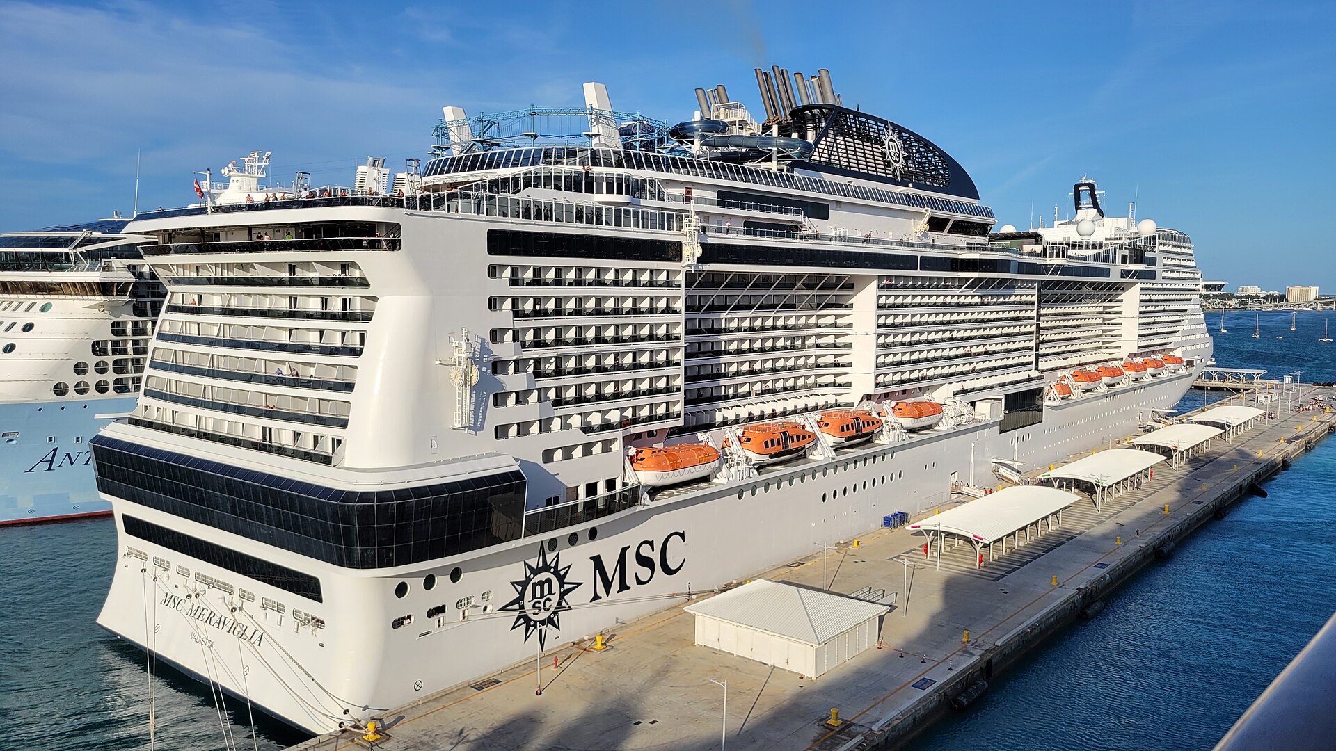 Stern of the MSC Meraviglia cruise ship with orange lifeboats docked at Nassau Cruise Port under a blue sky