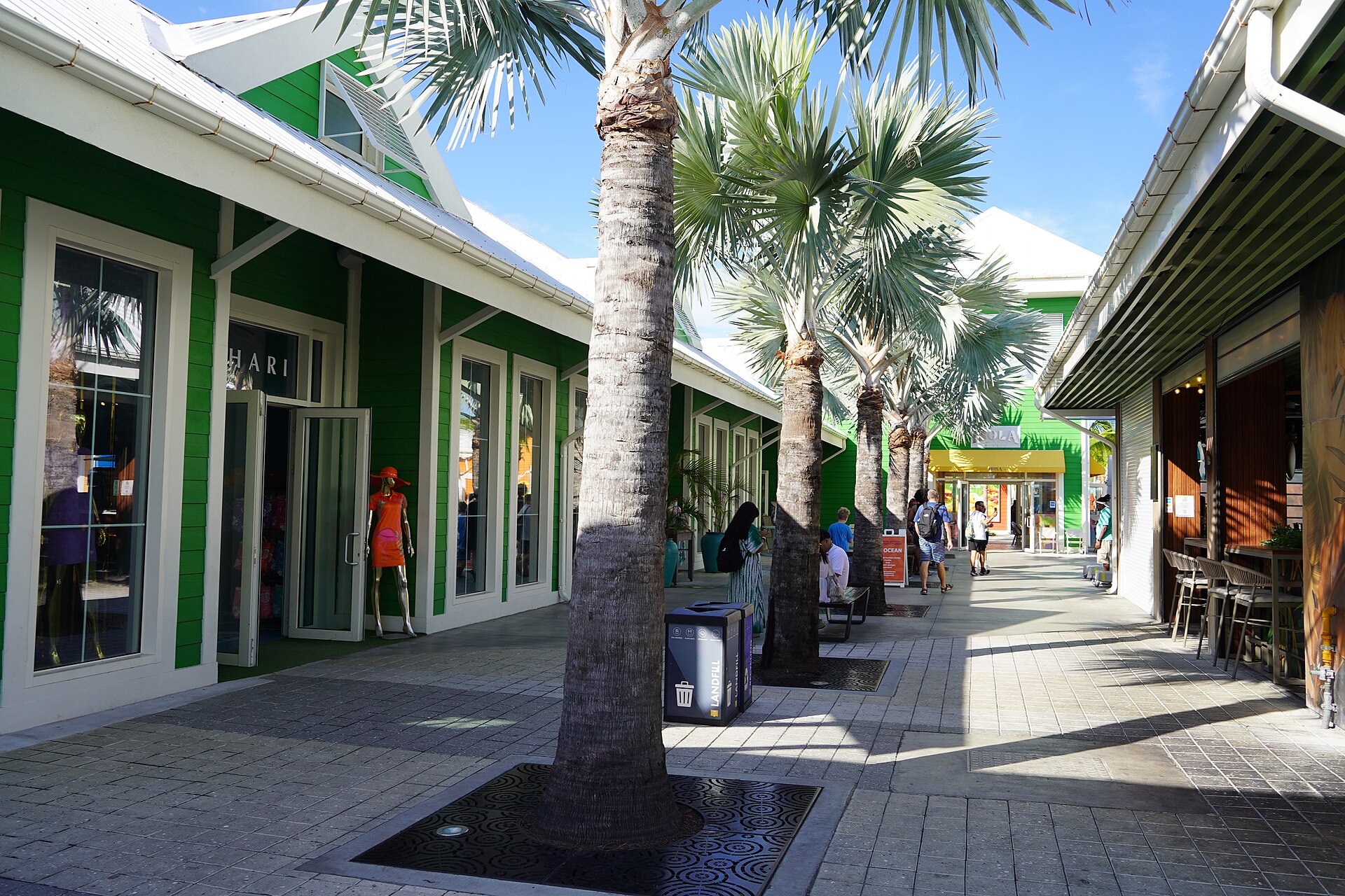 Green shopfronts and palm trees along a sunny walkway at Nassau Cruise Port