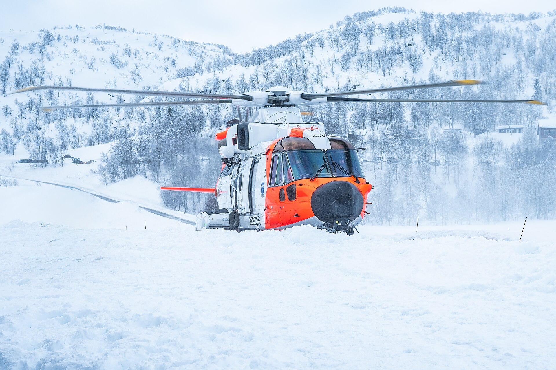 Orange and white Norwegian AW101 SAR Queen rescue helicopter landing on snow