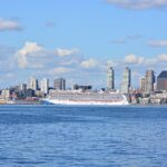 A Norwegian Cruise Line ship docked at Pier 66 on Seattle's waterfront, with the Space Needle and skyline under a blue sky