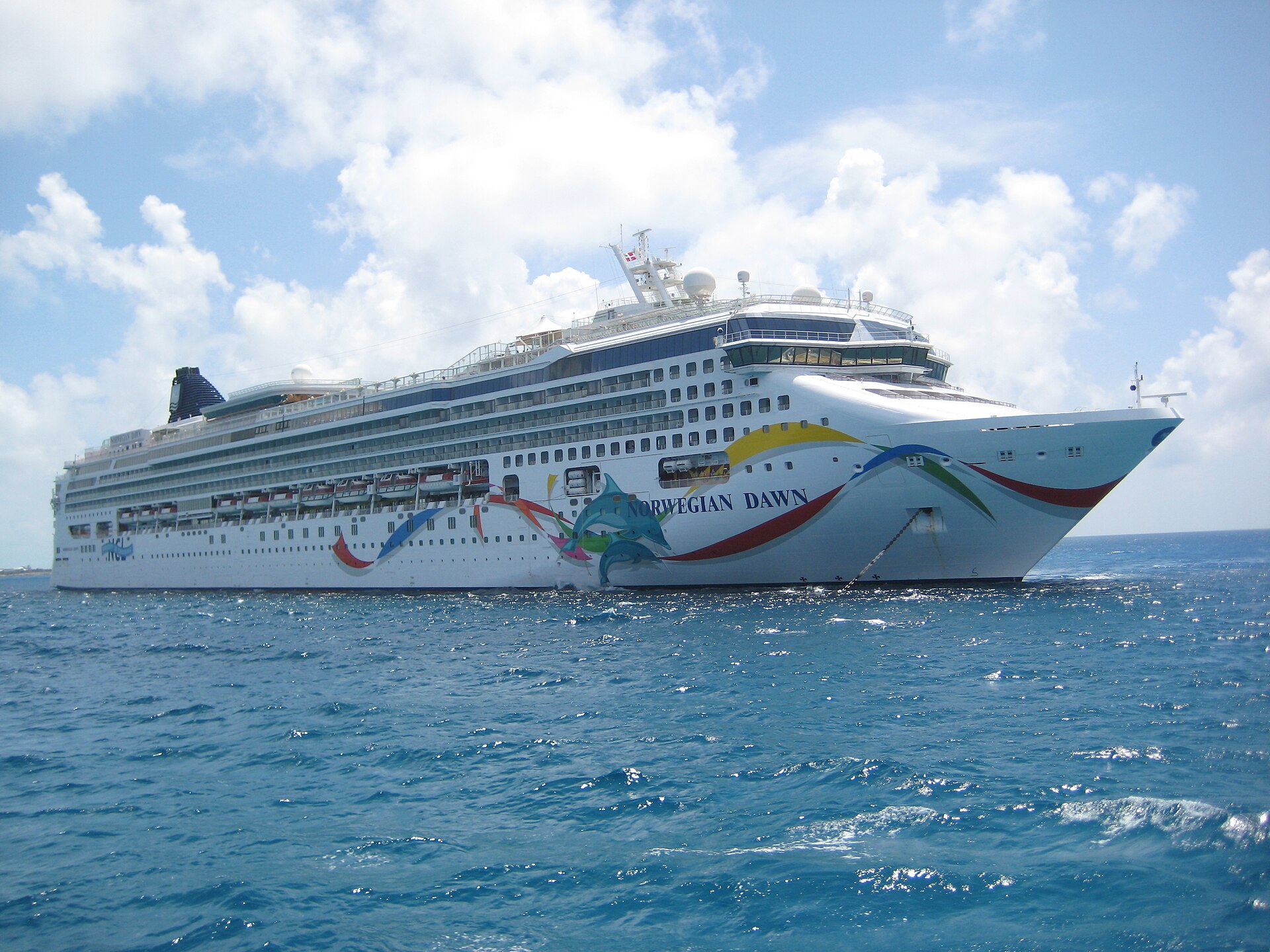Norwegian Dawn with its colourful hull art anchored in bright blue water off Great Stirrup Cay in the Bahamas