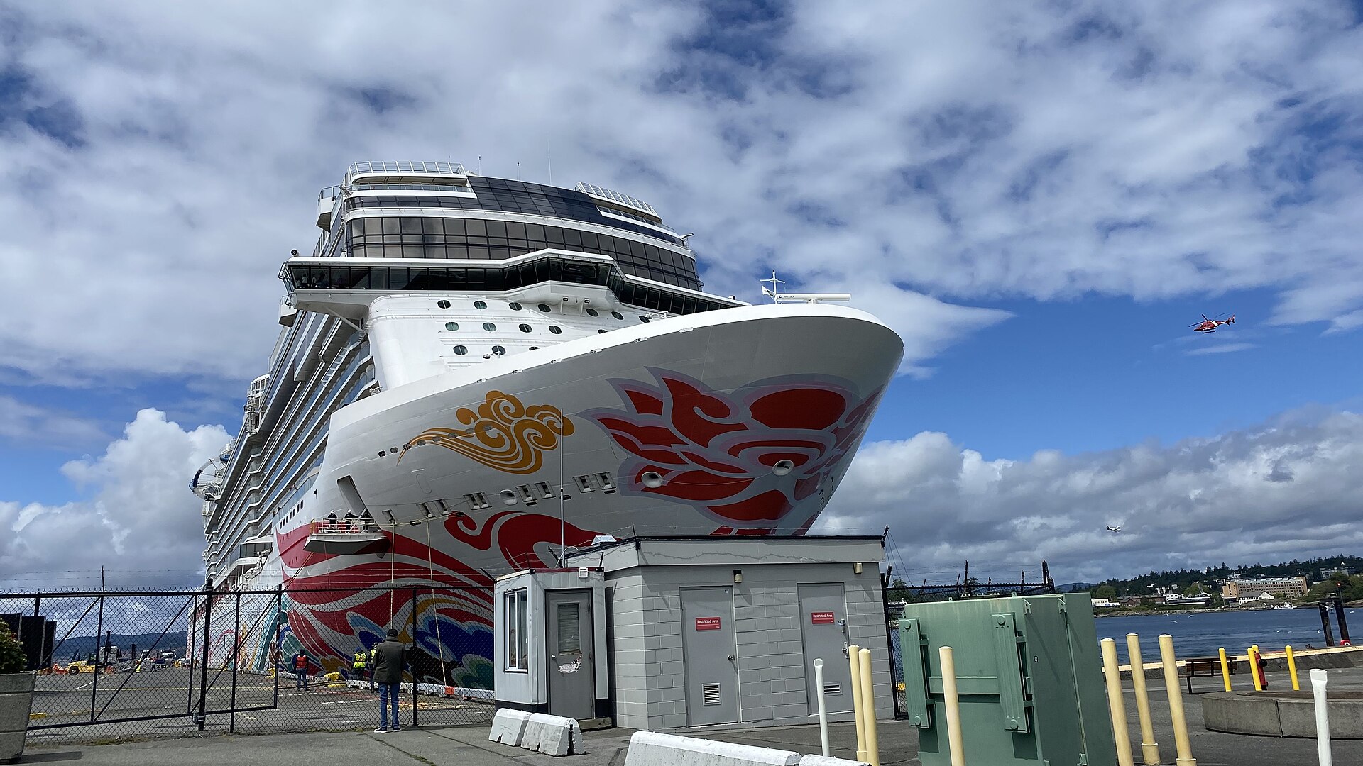 The bow of Norwegian Joy with its red and gold hull art, docked under a blue sky