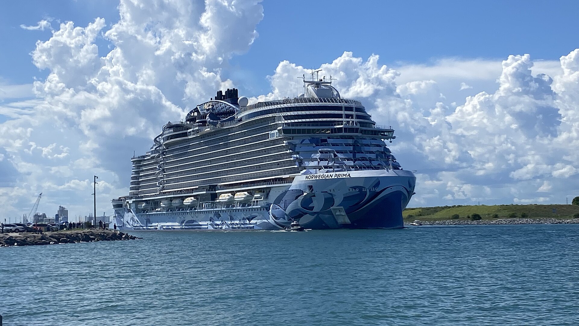 Norwegian Prima with its blue hull art sailing out of Port Canaveral under a bright sky with white clouds