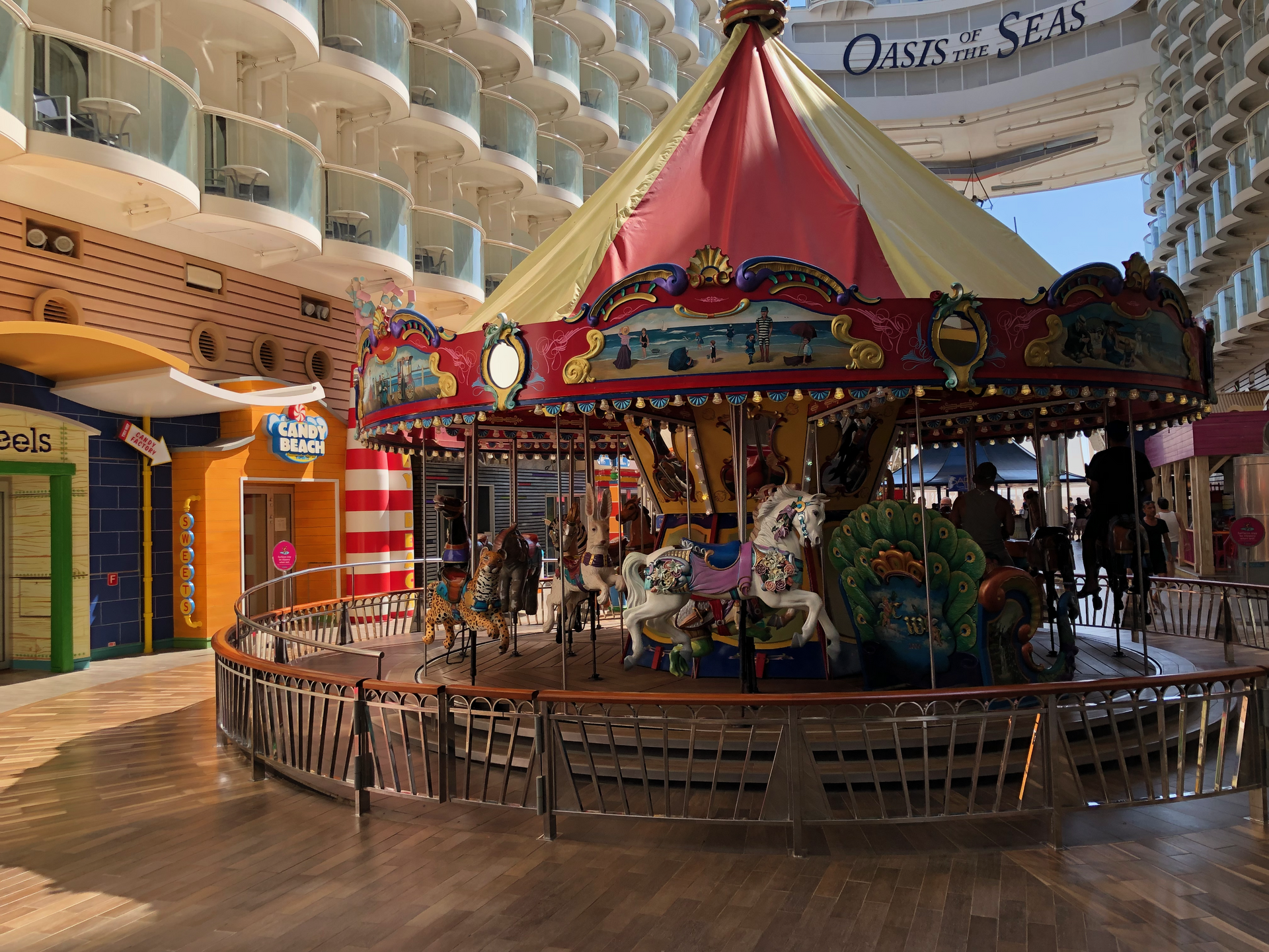 A colourful red and gold carousel with painted horses on the Boardwalk of Oasis of the Seas, with cabin balconies above