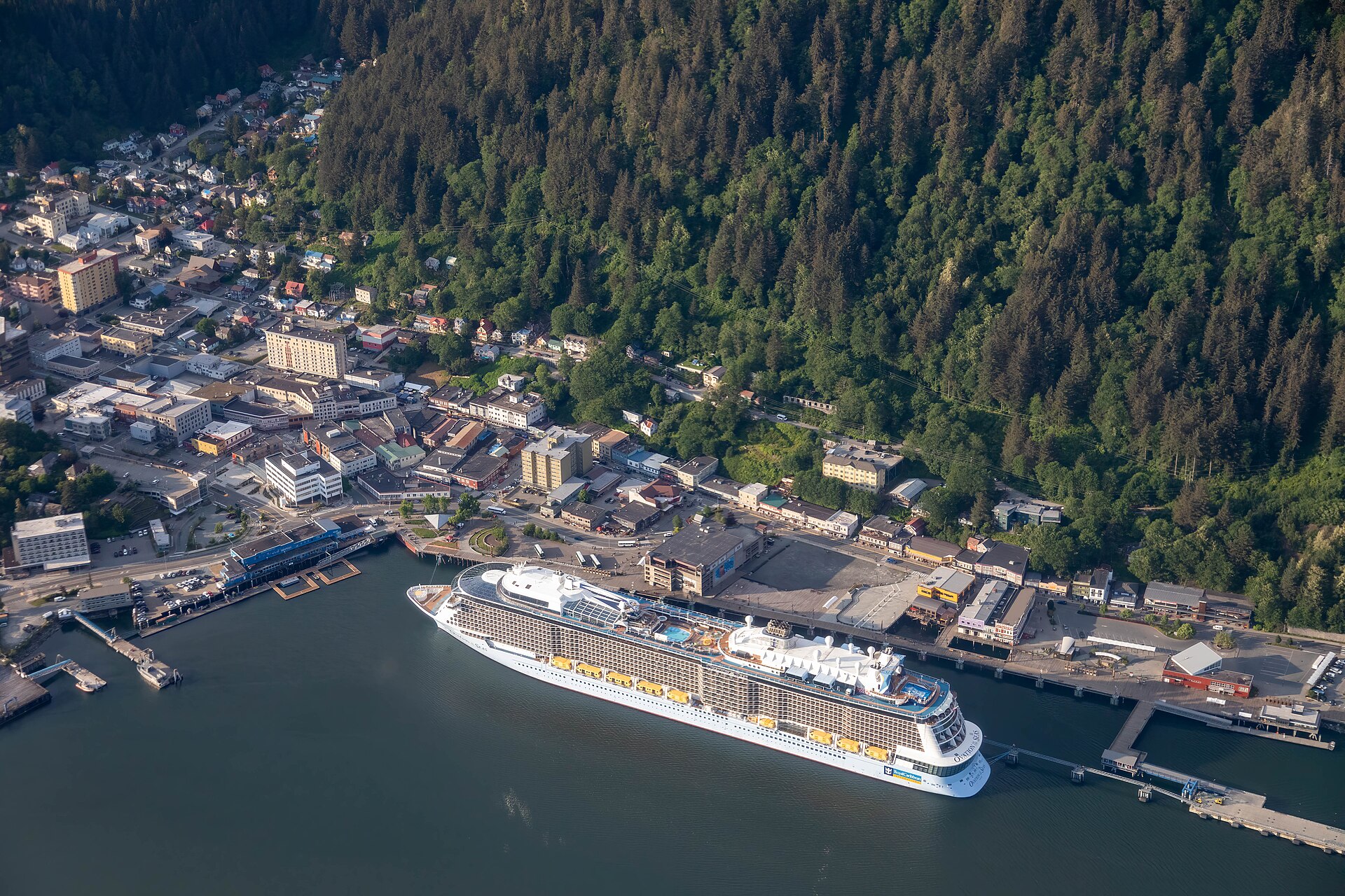 Aerial view of Ovation of the Seas docked in Juneau, Alaska, below a steep forested mountainside