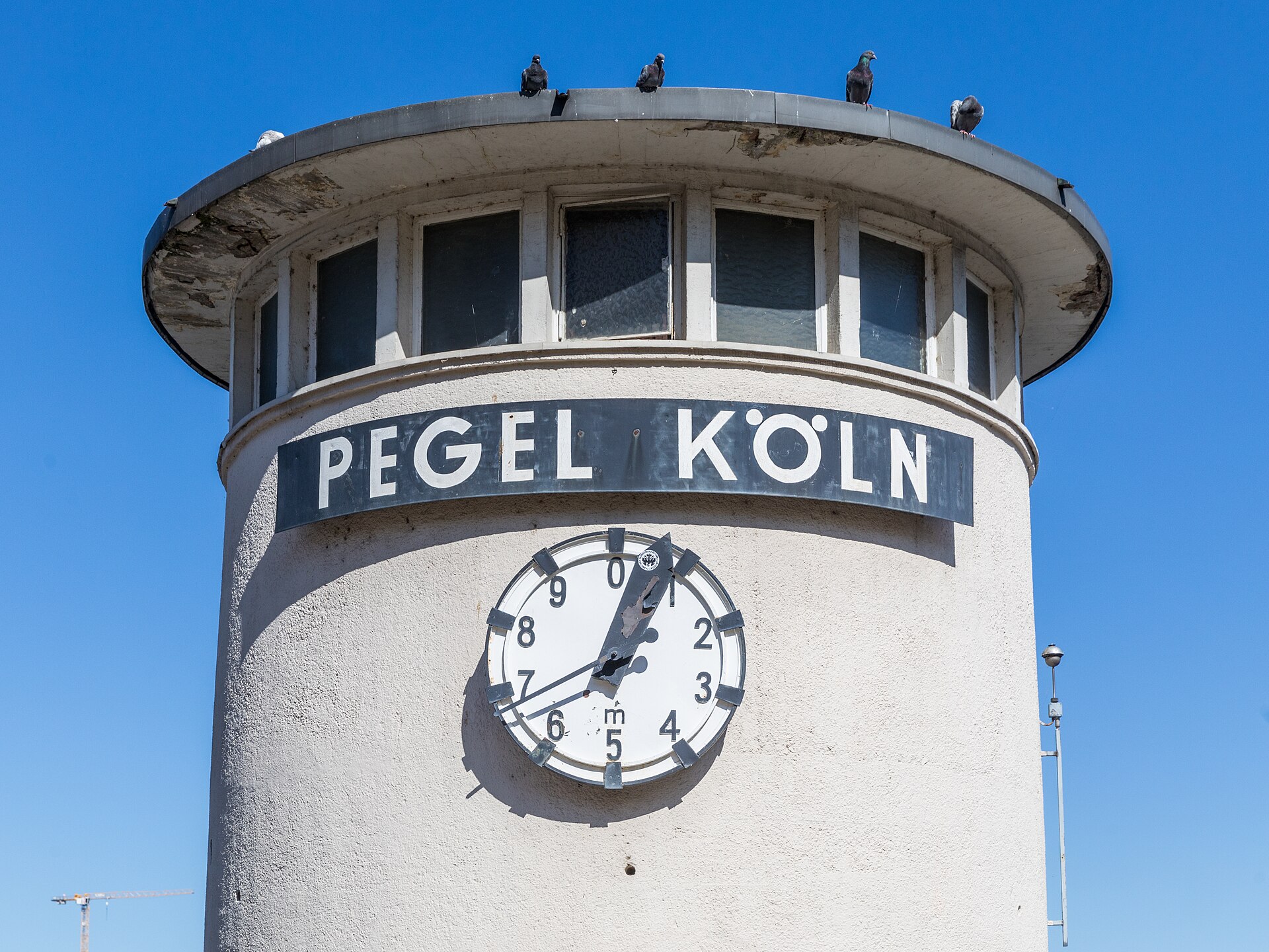 The Pegel Koeln gauge tower in Cologne with its clock-style water level dial against a bright blue sky