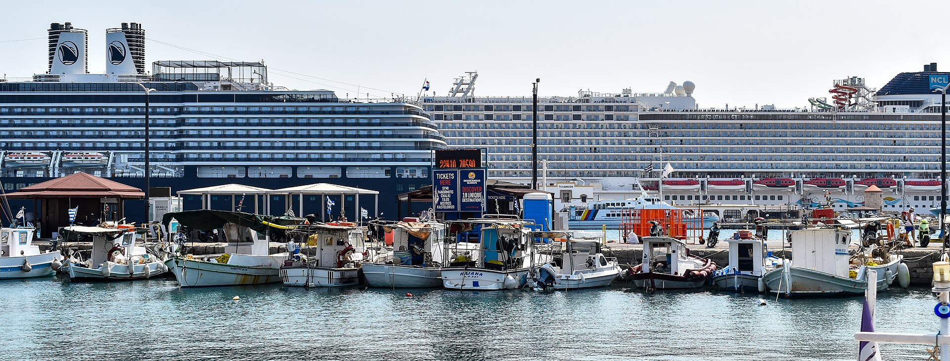 Two large cruise ships moored behind a row of small fishing boats in the Port of Rhodes