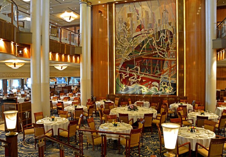 The Britannia Restaurant on Queen Mary 2, with round tables in white linen, honey-coloured chairs and a huge Art Deco mural of a liner in New York