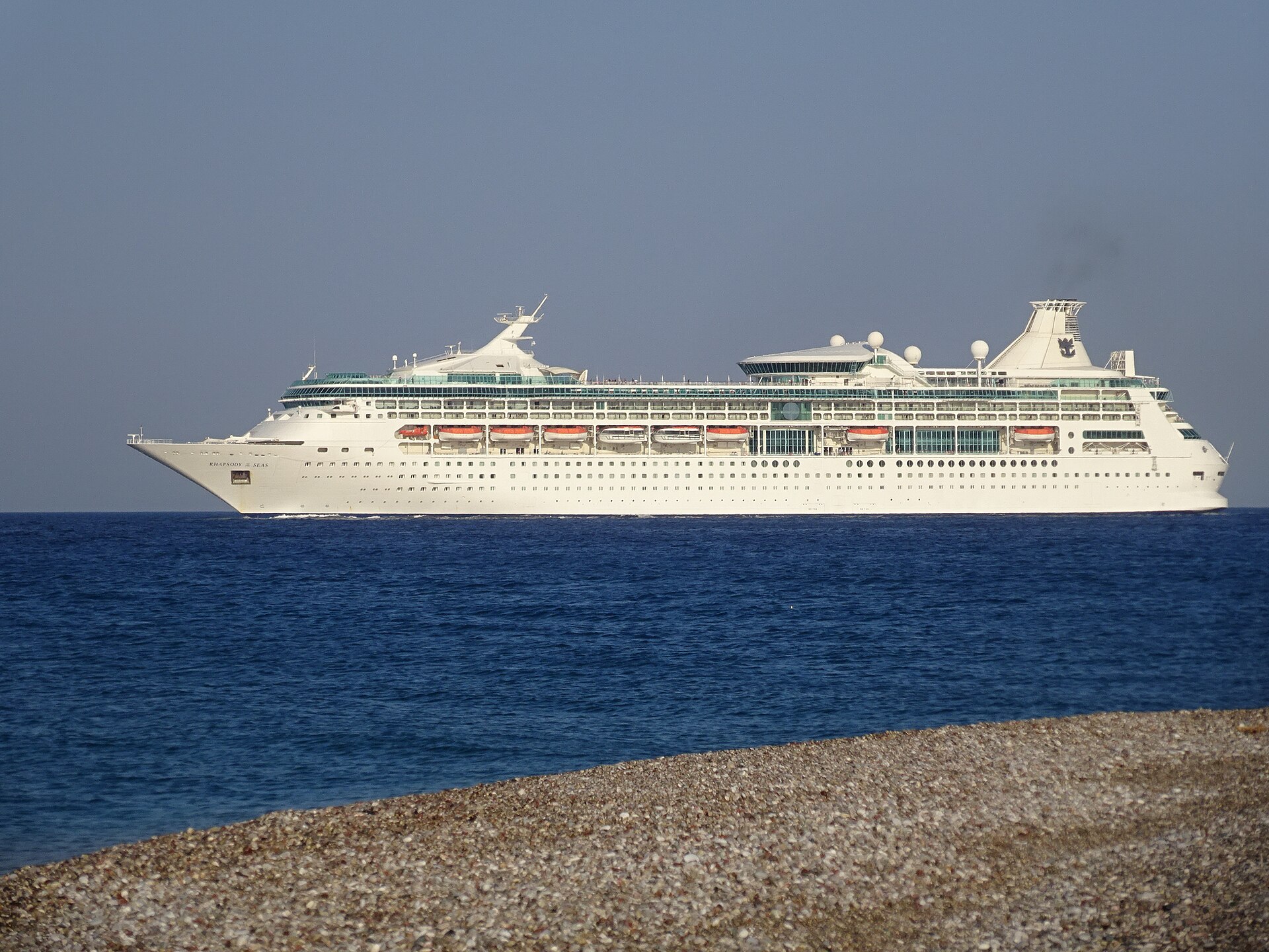 Rhapsody of the Seas sailing on a deep blue Aegean Sea past a pebble beach in Rhodes