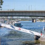 A Viking river cruise gangway slopes steeply down to a pontoon on the low Rhine in Cologne, with the Deutz Bridge behind