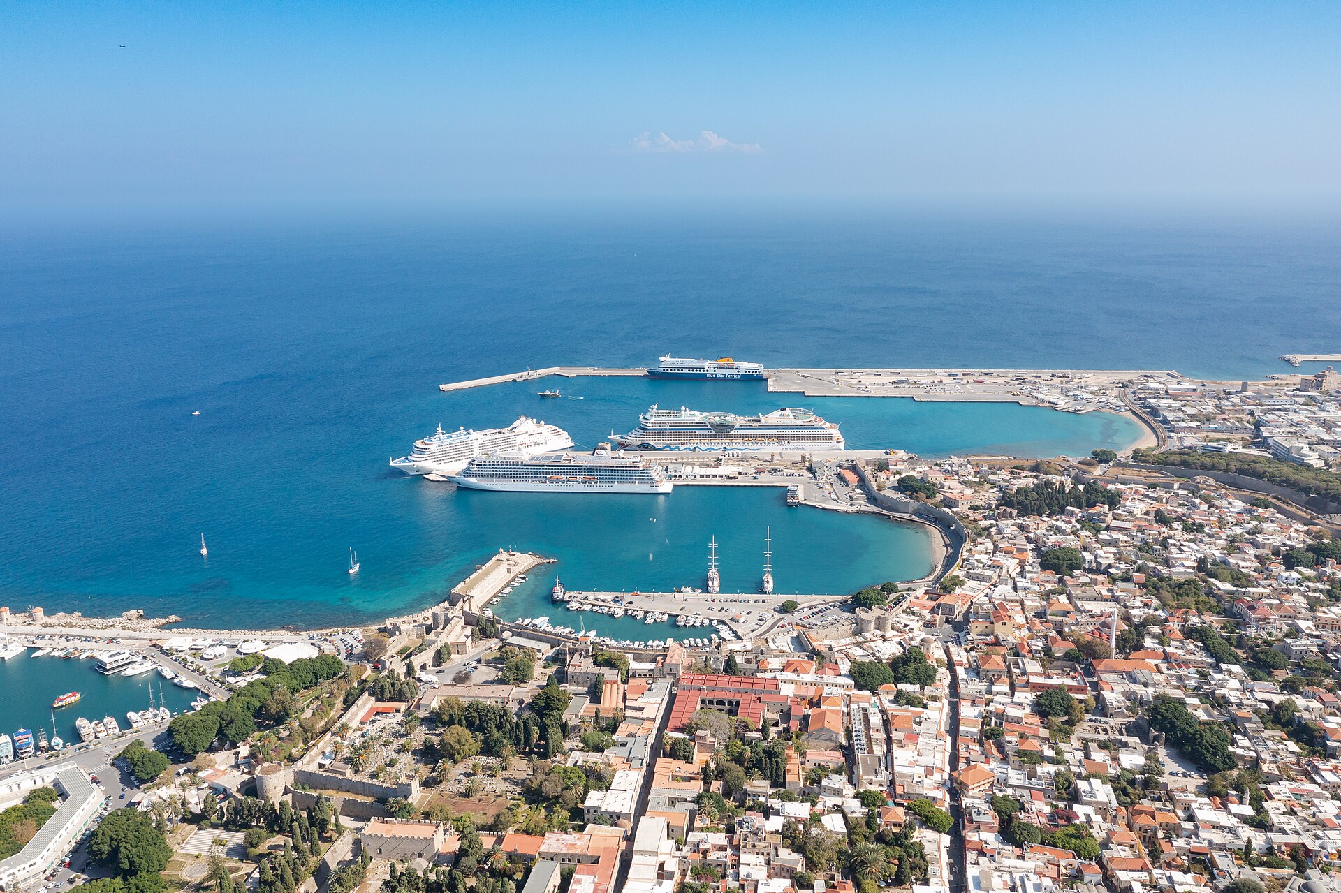 Aerial view of Rhodes harbour with three cruise ships at the breakwater, turquoise water and the Old Town rooftops