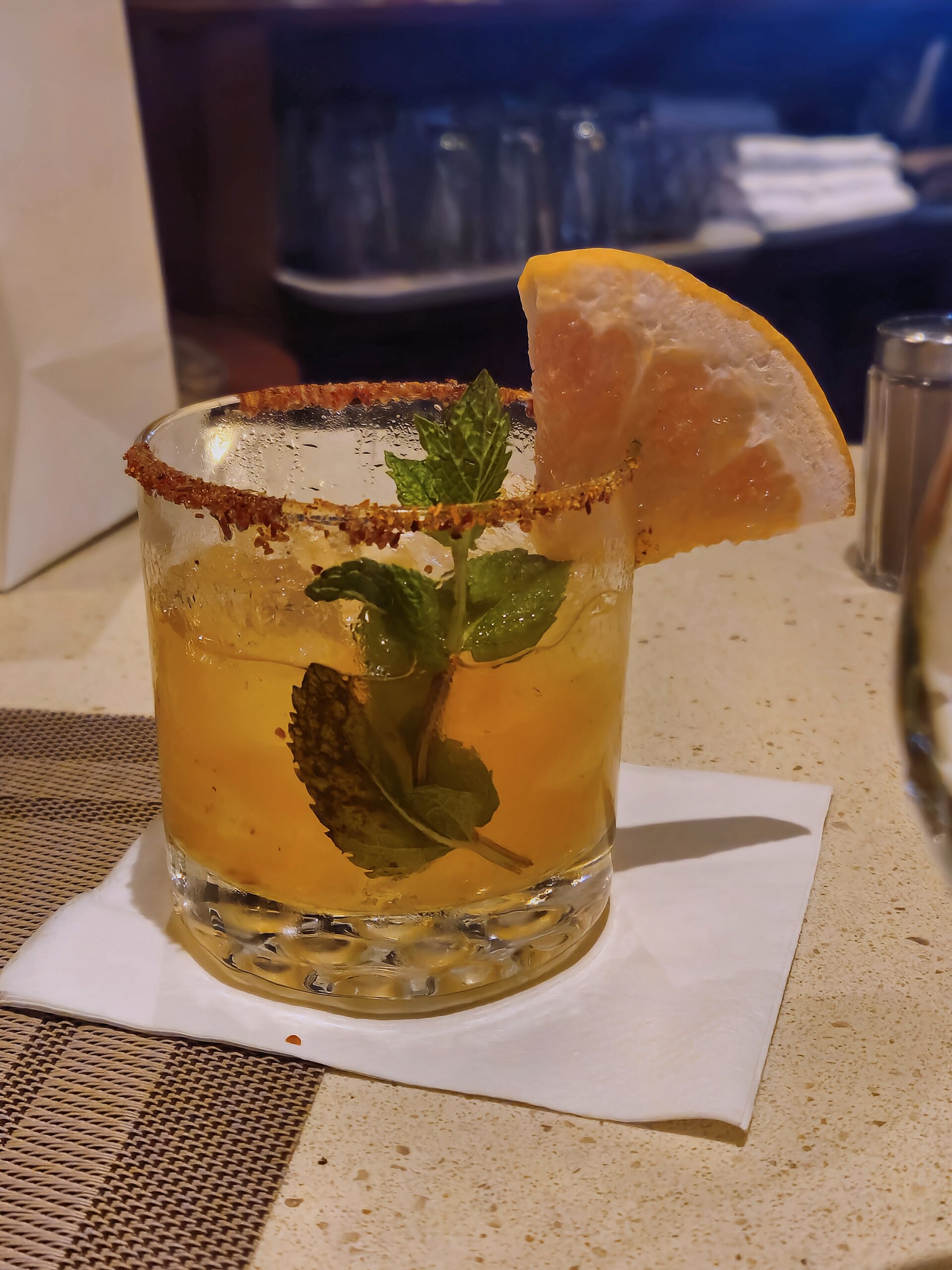 Spicy paloma cocktail with a grapefruit slice, mint and chili-salt rim on a bar aboard Ruby Princess