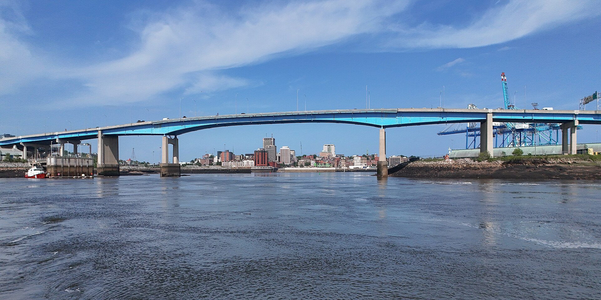 The blue Saint John Harbour Bridge spanning the harbour, with the uptown Saint John skyline behind it under a blue sky