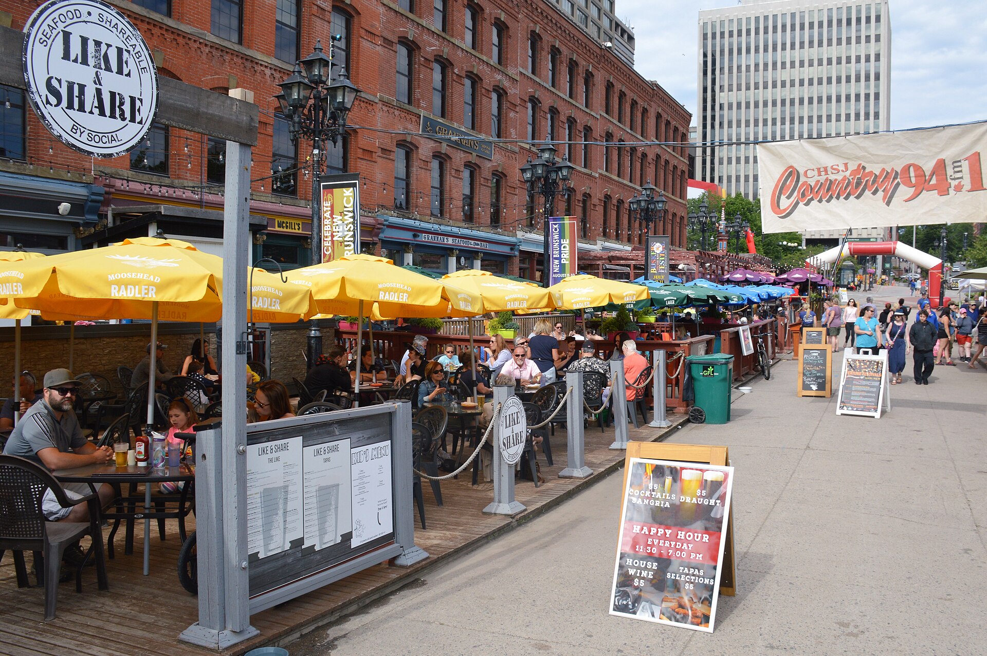 Busy outdoor patios with yellow umbrellas along the Market Square waterfront boardwalk in Saint John, New Brunswick