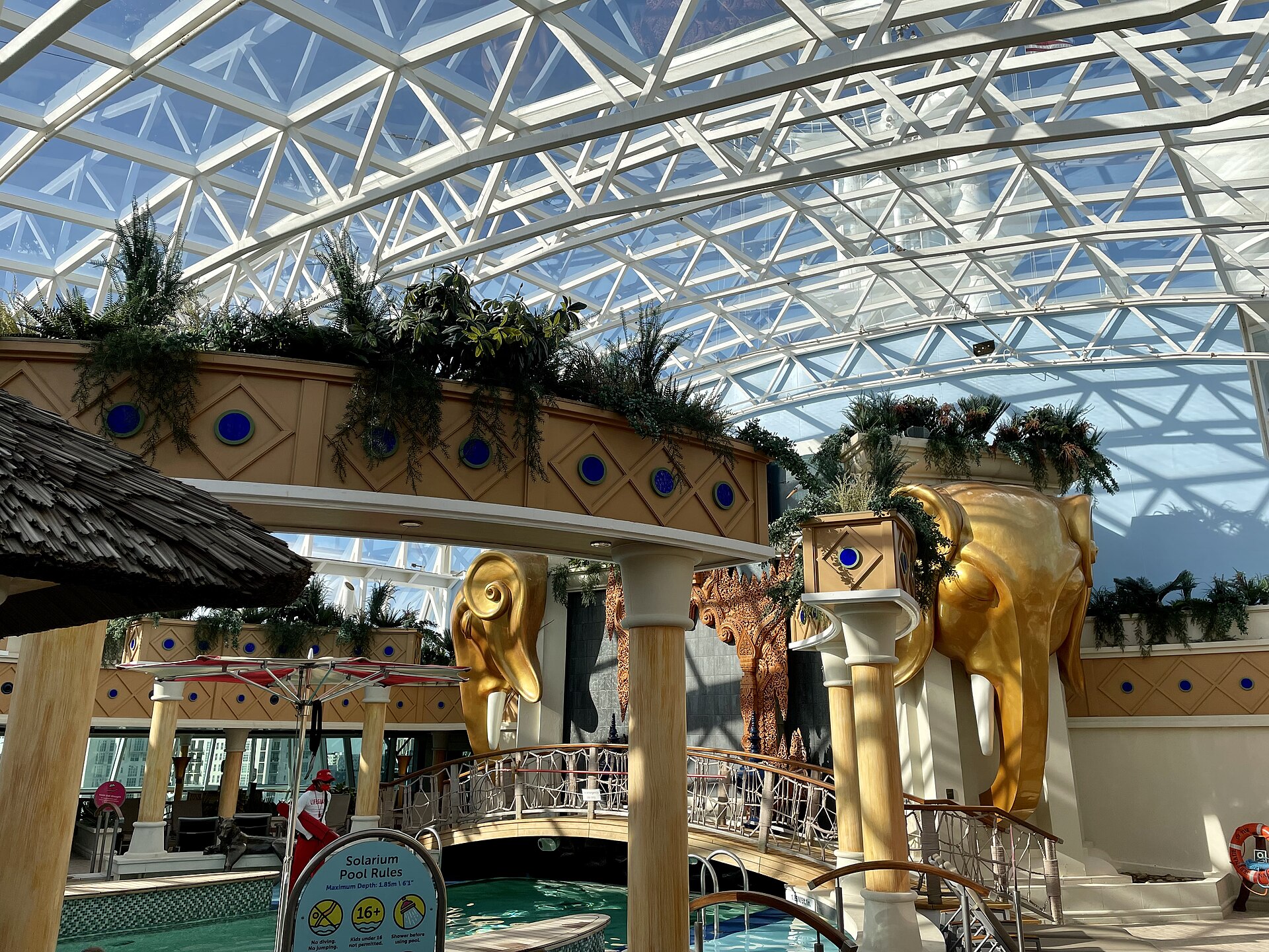 Glass-roofed adults-only Solarium on Serenade of the Seas with golden elephant statues, plants and a pool