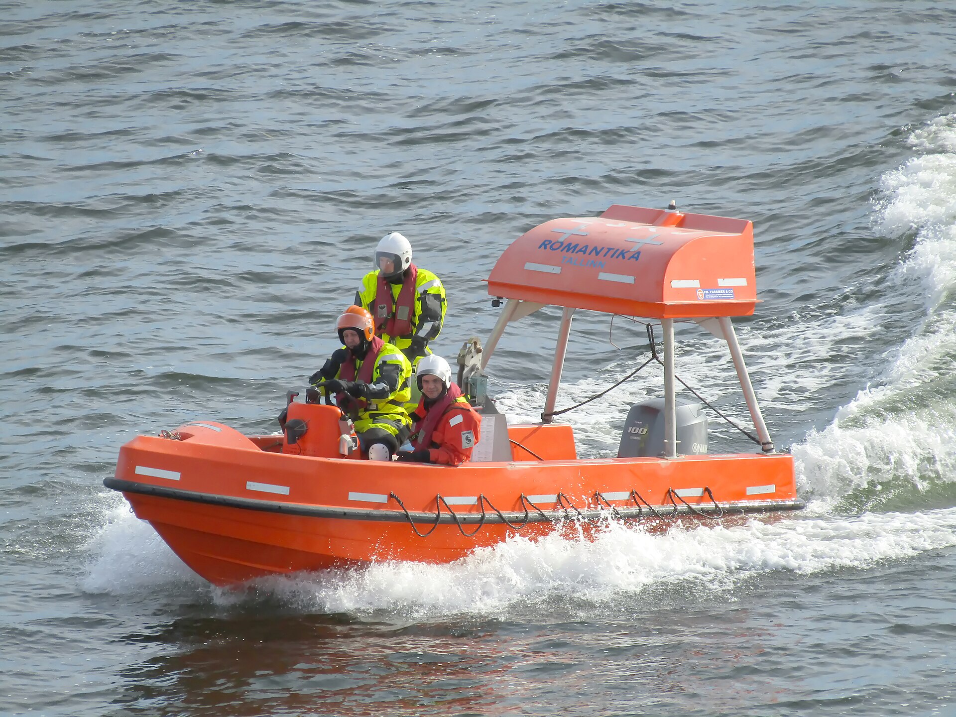 Bright orange man-overboard rescue boat with three crew speeding across the water