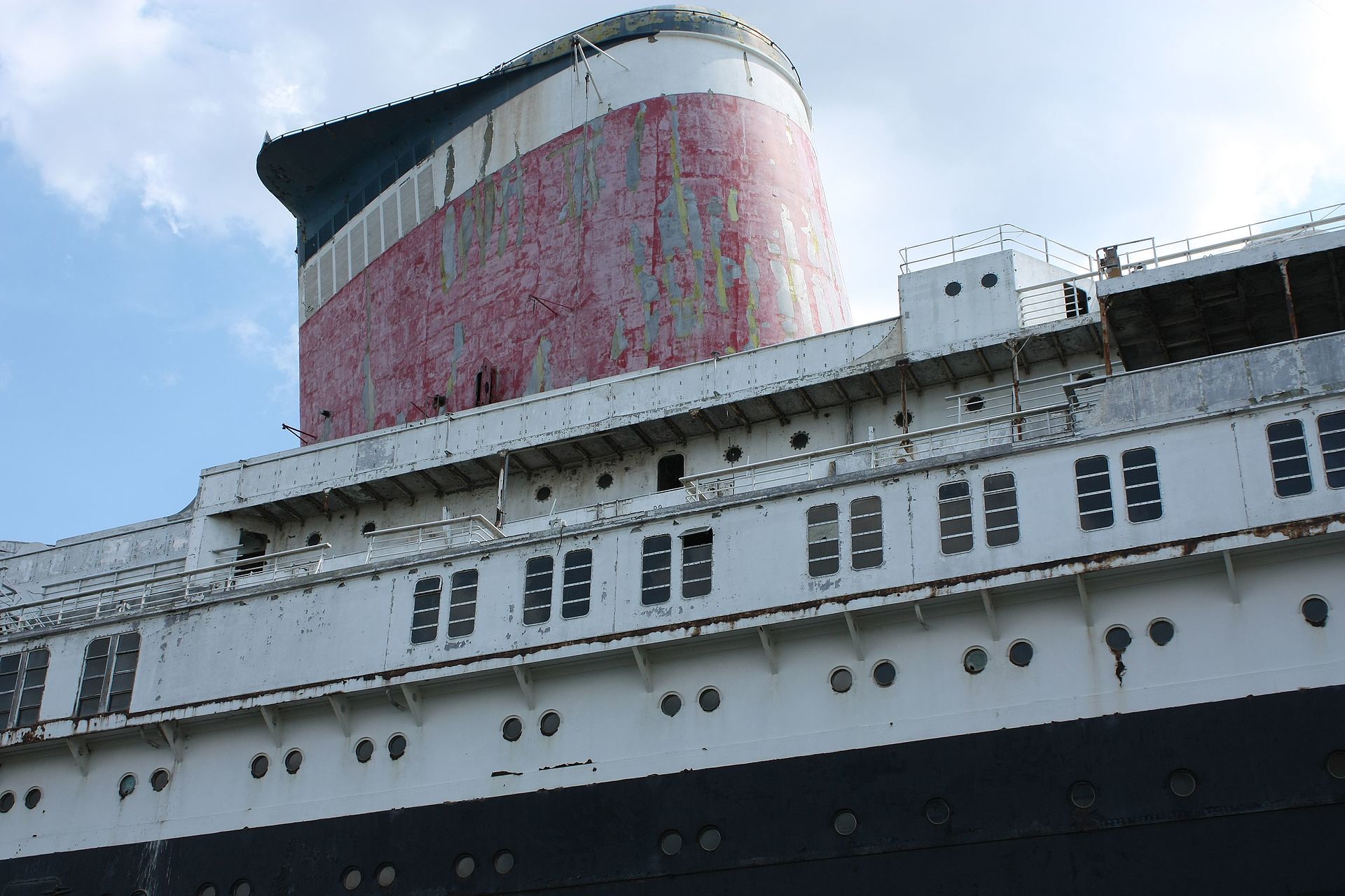 Close-up of the SS United States' faded red funnel and white superstructure against a blue sky