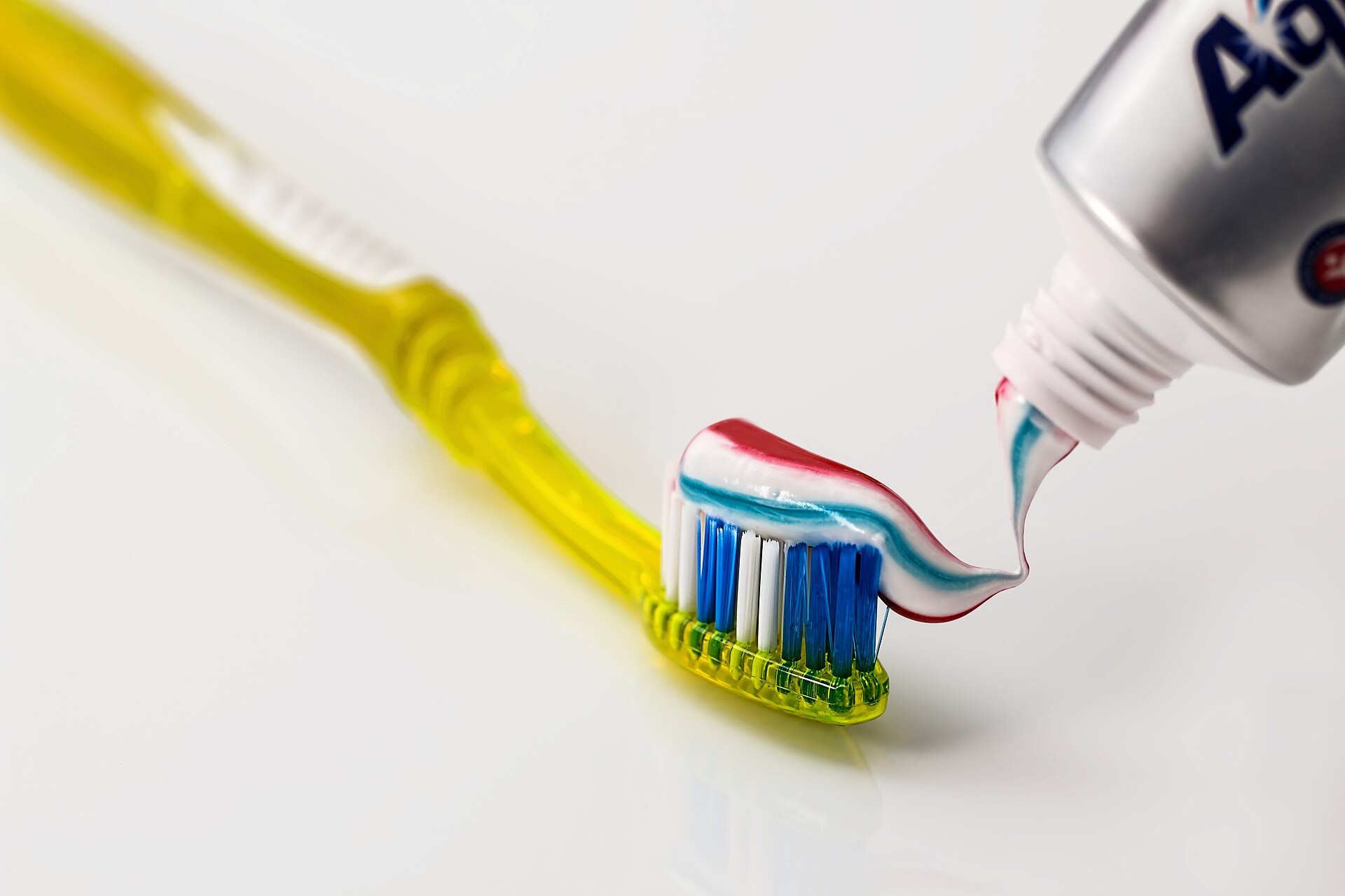 A yellow toothbrush with blue bristles and a stripe of red, white and blue toothpaste