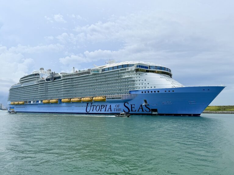 Royal Caribbean's Utopia of the Seas sailing out through the Port Canaveral channel under a blue sky