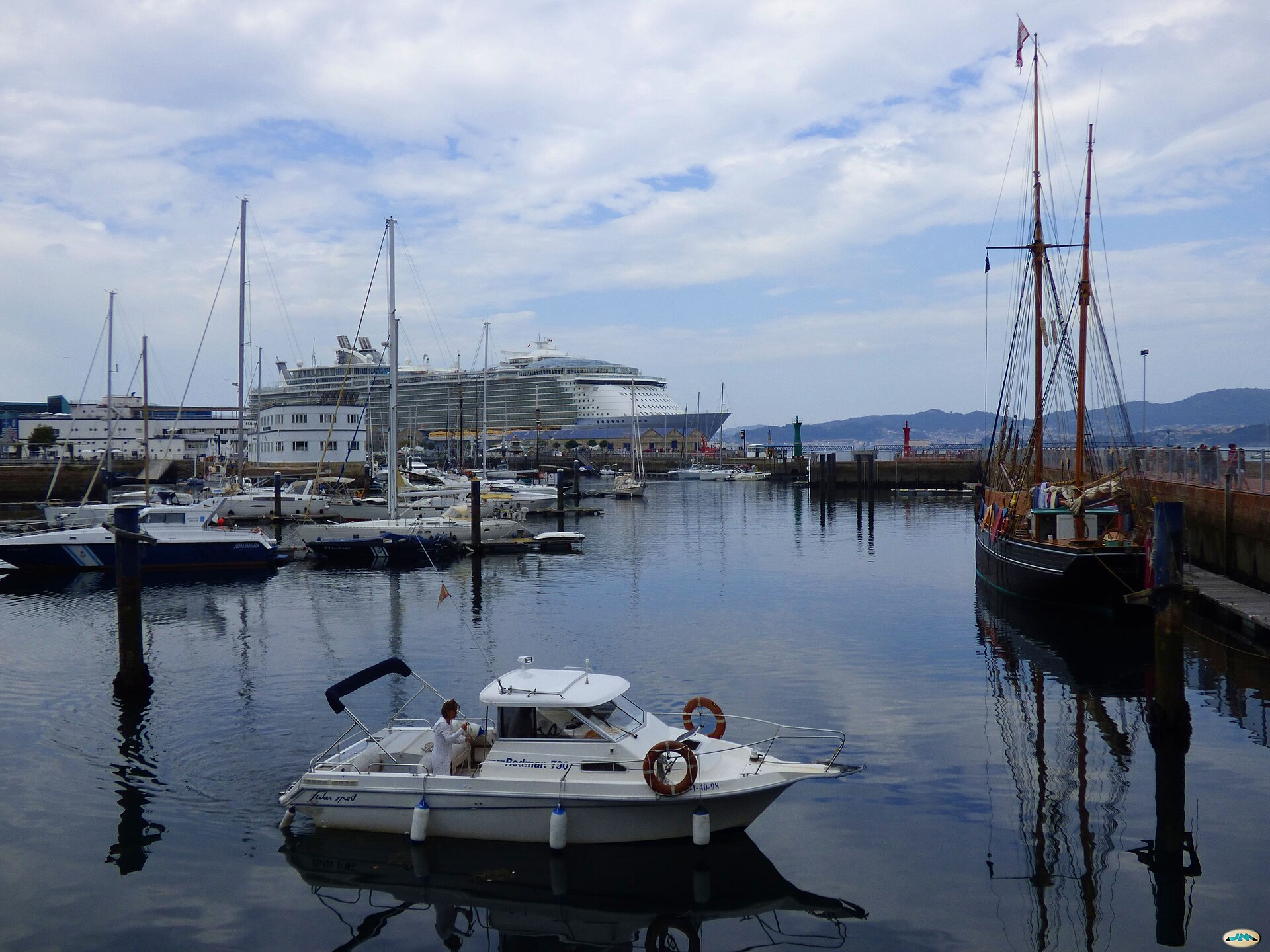 A large cruise ship docked beyond the marina and sailboats in the port of Vigo, Spain