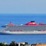 Virgin Voyages cruise ship Scarlet Lady sailing on a deep blue sea, with her red funnel and Virgin logo